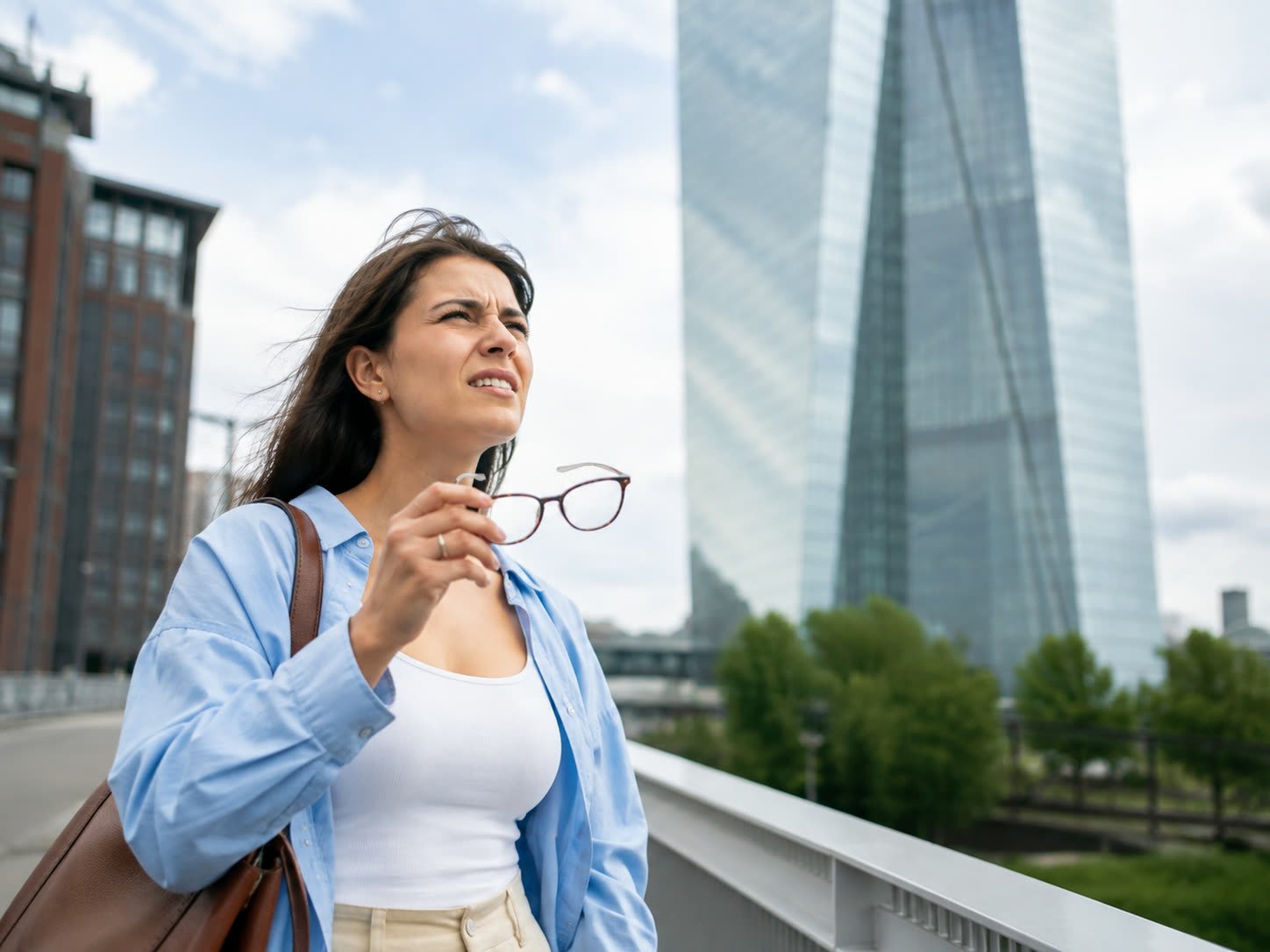 Junge Frau mit Kurzsichtigkeit blinzelt in die Ferne und hält ihre Brille in der Hand.